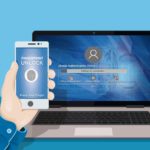 Hand hält Smartphone vor Laptop mit Anmeldemaske